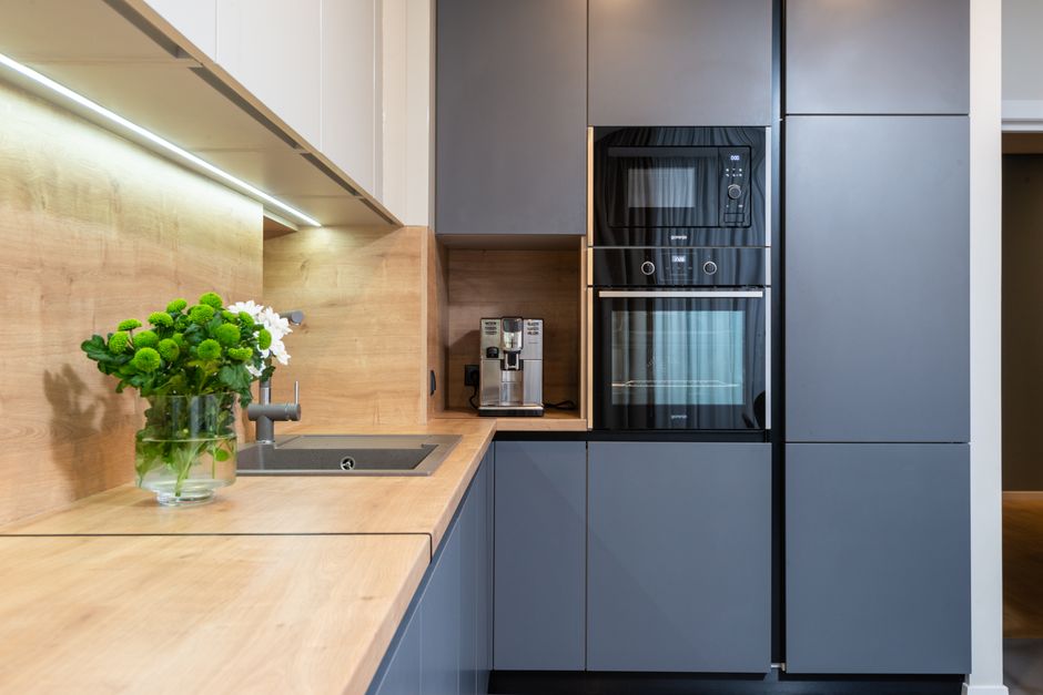 A modern kitchen corner featuring built-in appliances including a black oven with a glass door, a microwave oven beside it, and a small section of a dark countertop with a glossy finish. On the counte